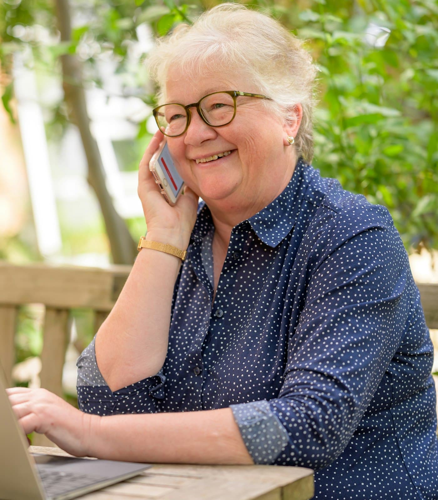 A smiling older woman chatting on the phone in her garden